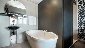 Un baño moderno con una bañera independiente, un lavabo de vidrio y un espejo grande sobre el lavabo.