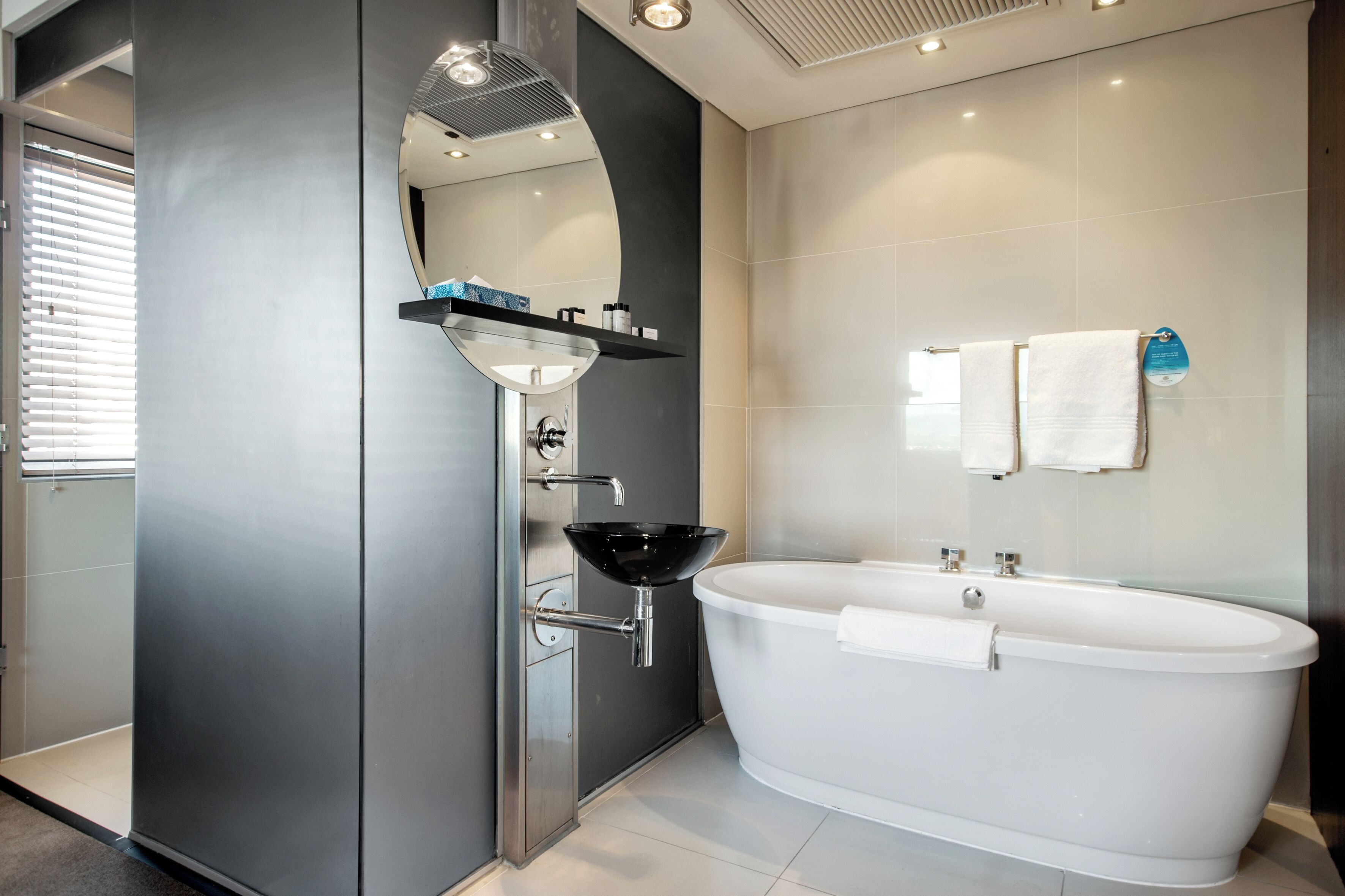 Un baño moderno con una bañera independiente, un lavamanos con cerramiento de vidrio y un espejo sobre el lavamanos.