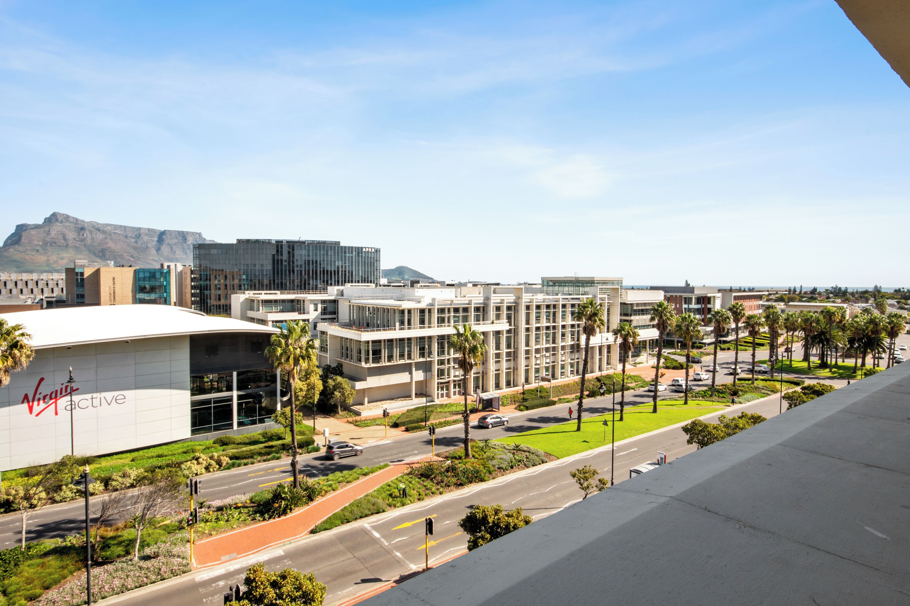 A modern building with a Virgin Active sign, surrounded by palm trees and a clear sky.