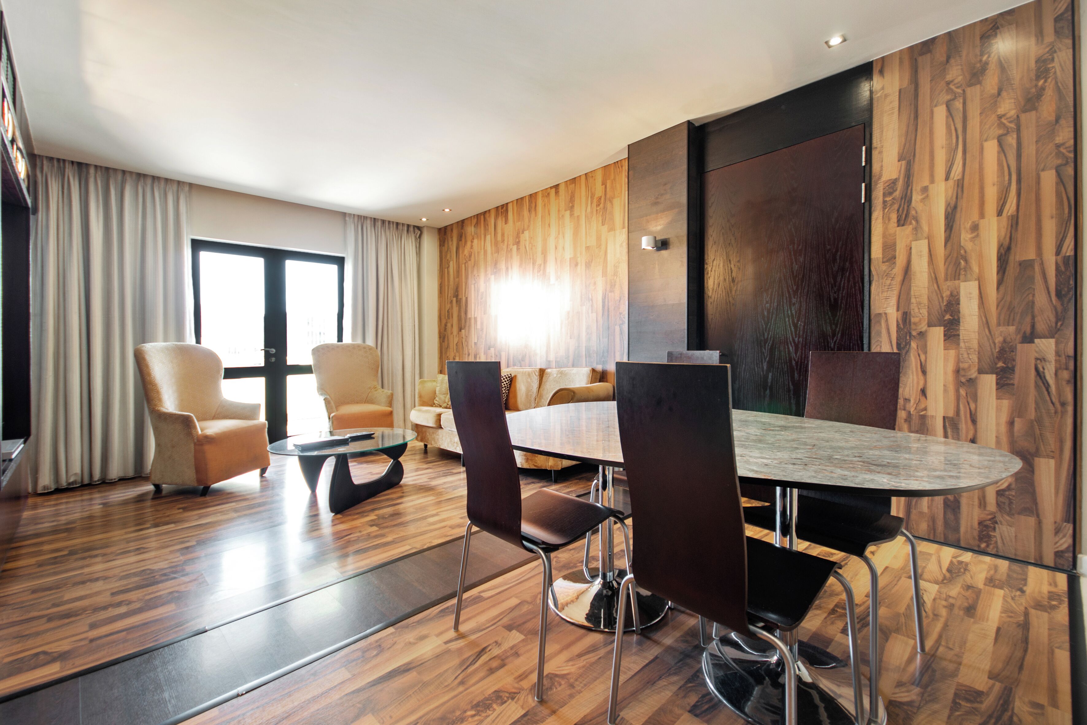 A modern hotel room with a wooden floor, a round dining table, and a sofa.