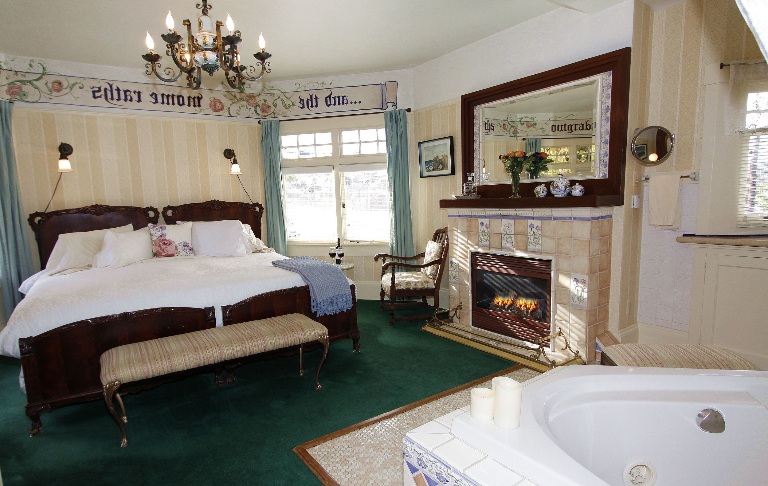 A bedroom with a large bed, a bench, a fireplace, and a bathtub.