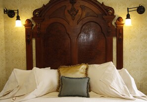 A bed with a wooden headboard, two wall-mounted lamps, and patterned wallpaper. - Jabberwock Inn (Monterey)