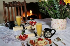 A breakfast setting with a table set for two, including plates of food, a pitcher of orange juice, a black mug, and a floral vase. - Jabberwock Inn (Monterey)