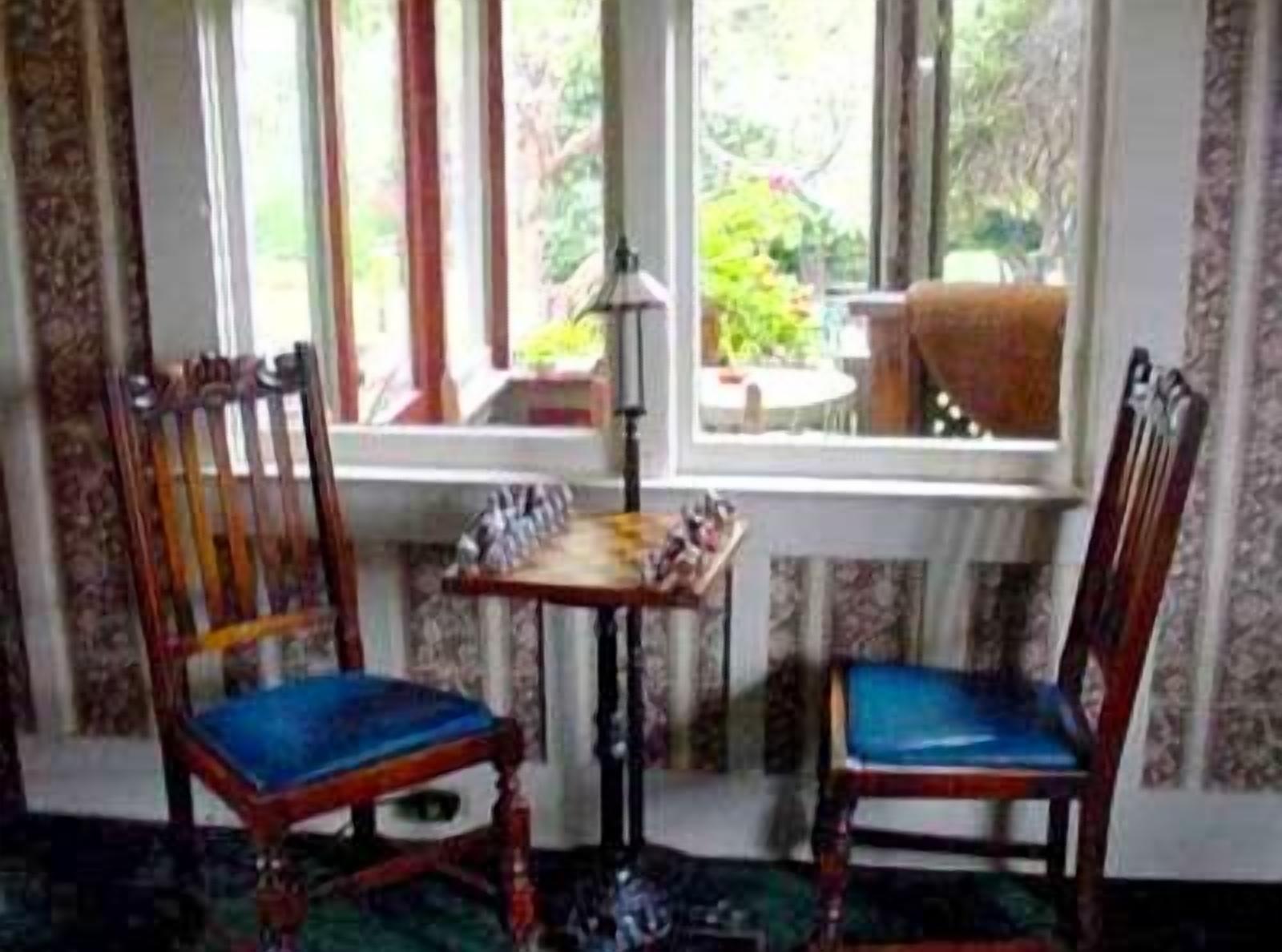 A room with two wooden chairs with blue cushions, a small table, and a window with a view of greenery outside.