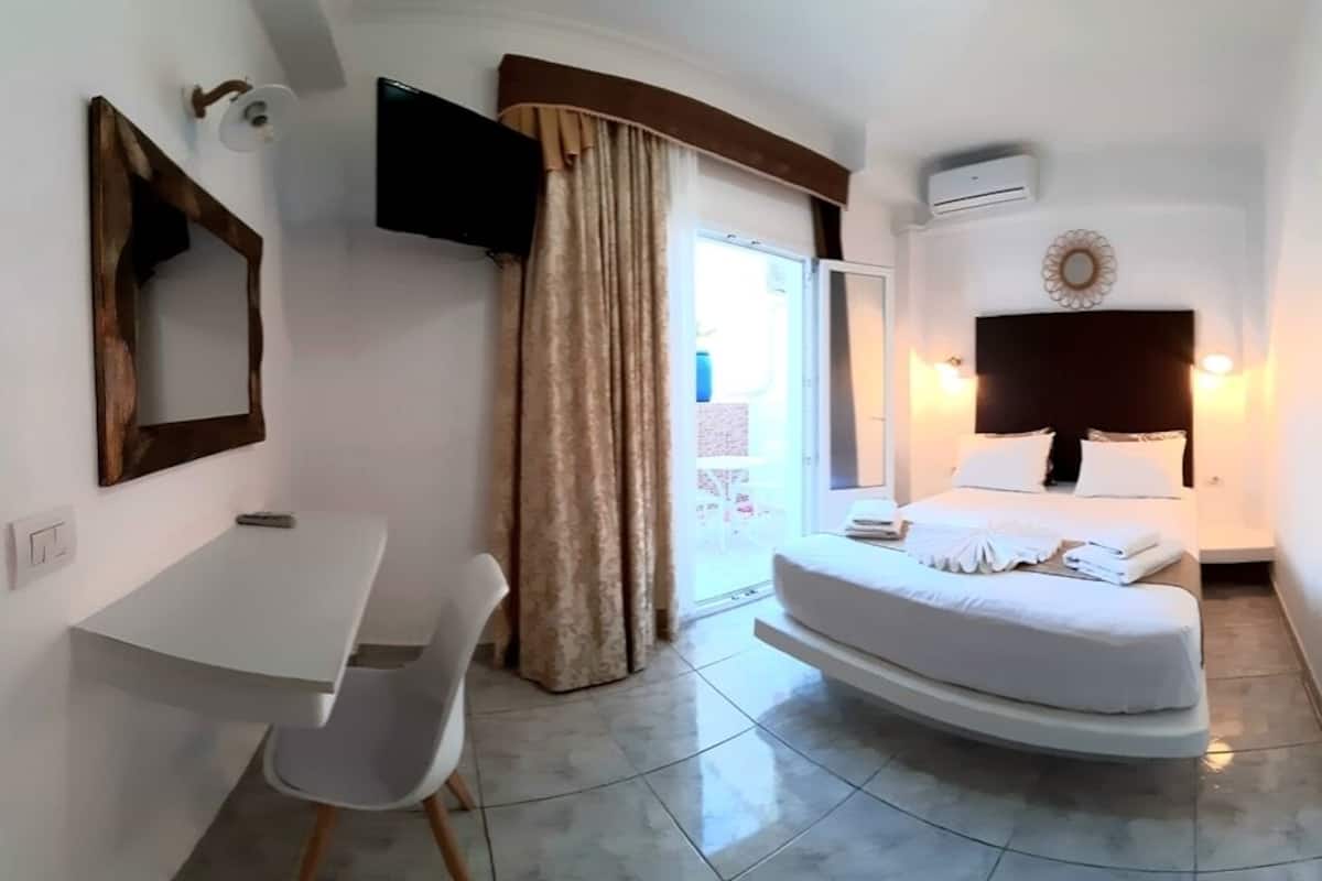 A bedroom with a bed, a desk, a chair, a TV, and a window with curtains.