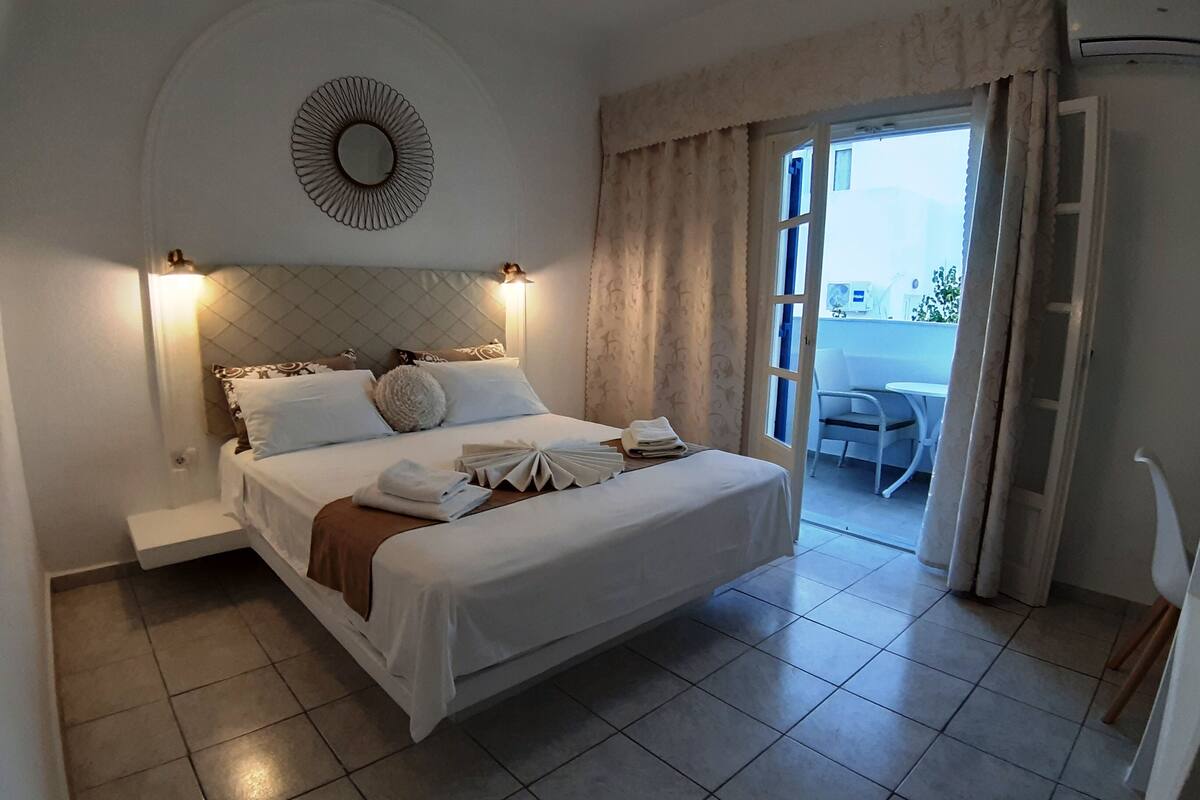 A neatly made bed with a headboard, a bedside table with a lamp, and a view of an outdoor area through a sliding door.