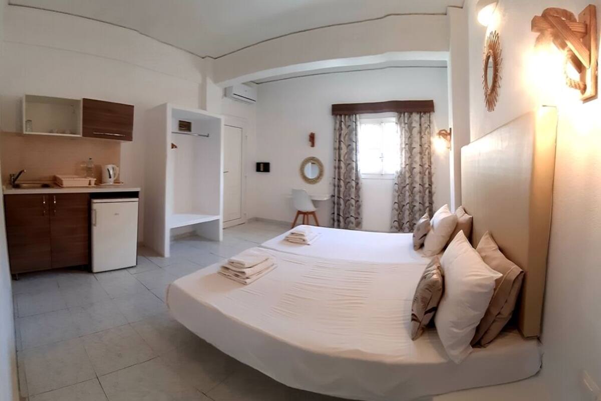 A bedroom with a large bed, a small kitchenette, and a bathroom.