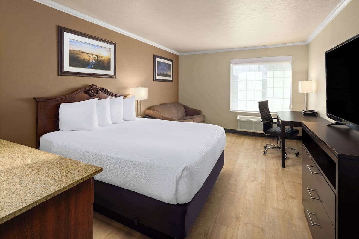 Ein Hotelzimmer mit einem großen Bett, einem Schreibtisch, einem Stuhl, einem Fernseher und zwei gerahmten Bildern an der Wand.