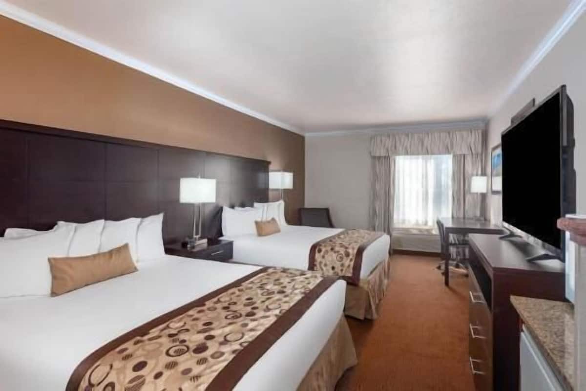 Ein Hotelzimmer mit zwei Betten, einem Schreibtisch, einem Fernseher und einem Fenster mit Vorhängen.