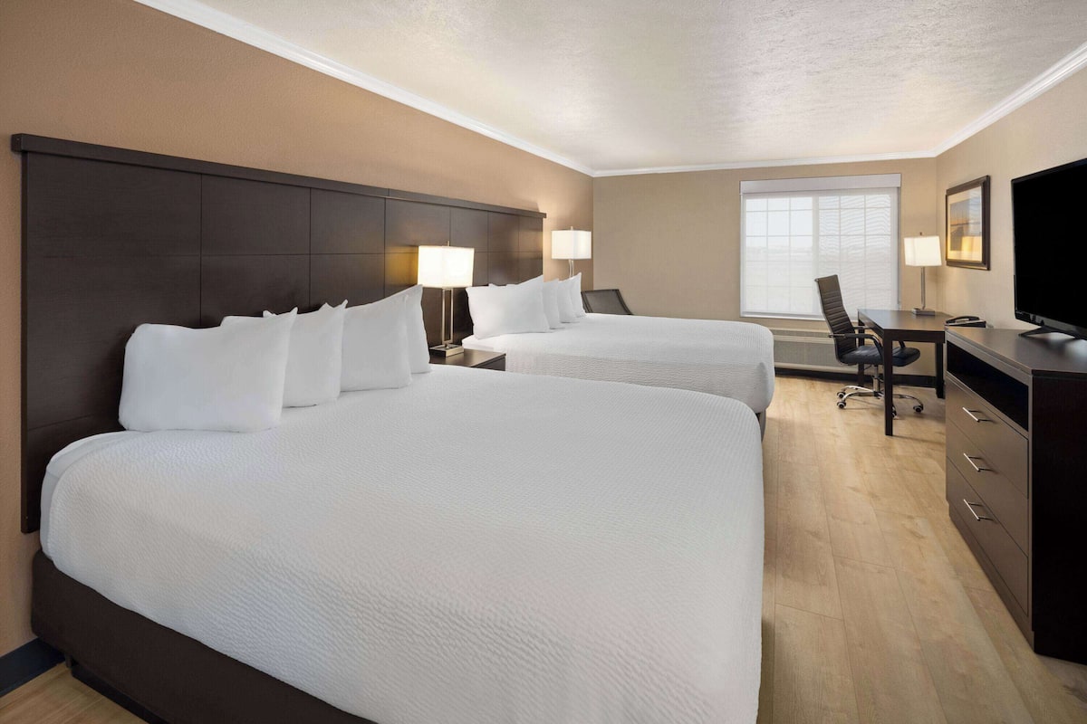 Ein Hotelzimmer mit zwei großen Betten, einem Schreibtisch, einem Sessel und einem Fernseher.