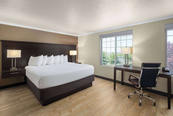 A hotel room with a large bed, a desk with a chair, two bedside lamps, and a window with a view.