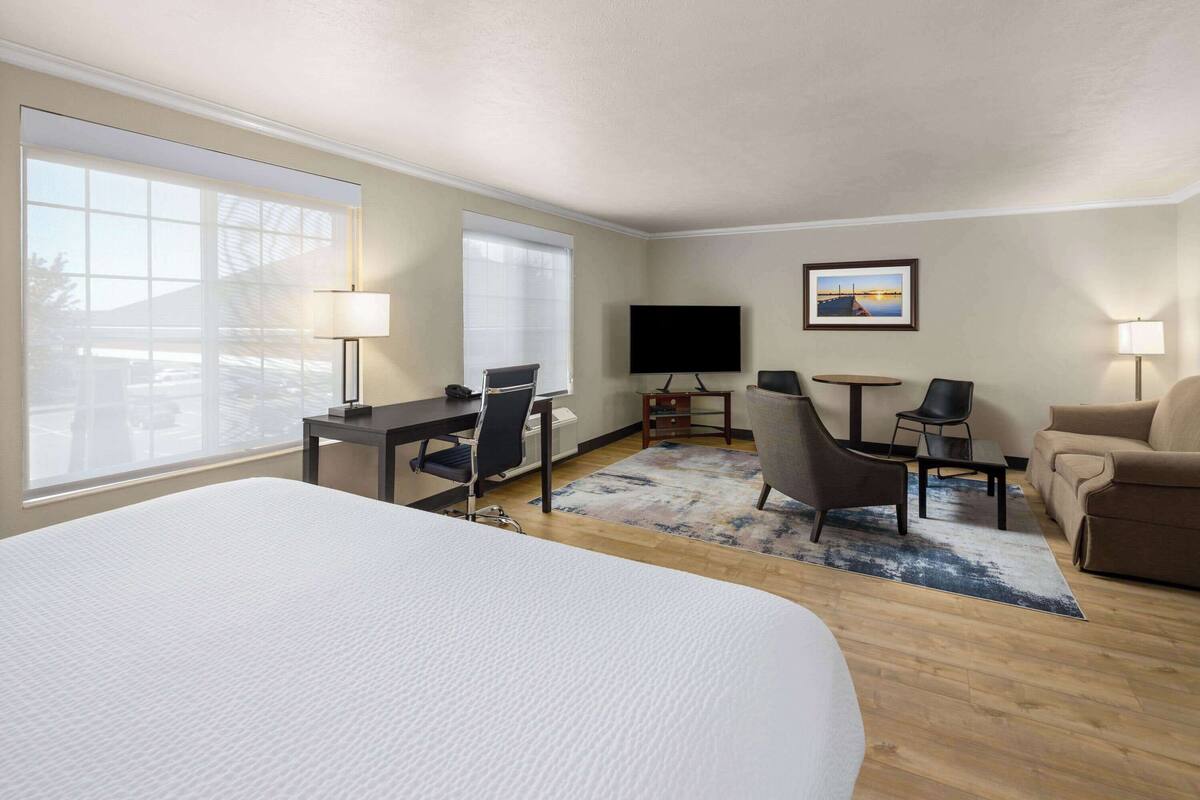 Ein Hotelzimmer mit einem großen Bett, einem Schreibtisch mit Stuhl, einem kleinen Tisch mit Stuhl, einer Couch, einem Fernseher und einem Fenster mit Blick ins Freie.