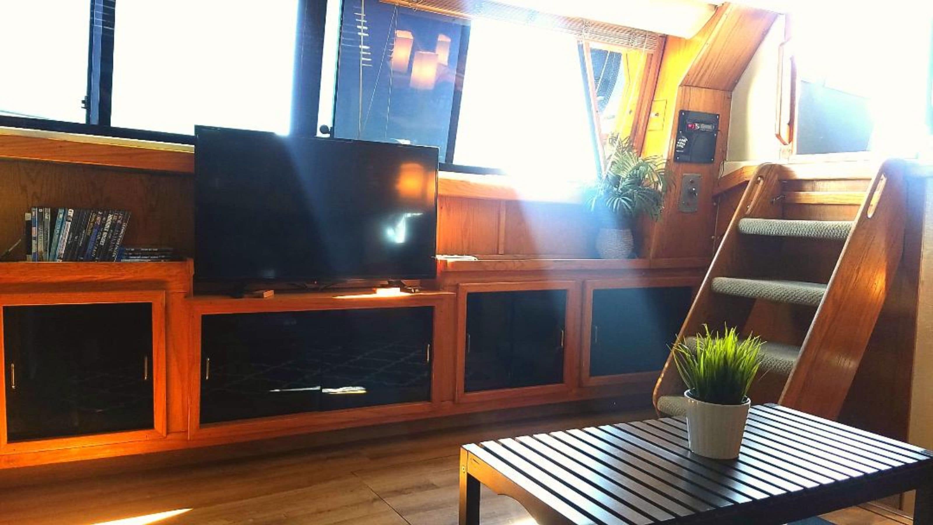A cozy living area with a television on a wooden cabinet, a small table with a plant, and a wooden staircase.