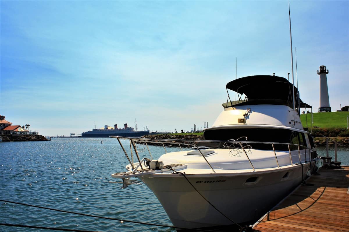A white yacht docked at a pier with a lighthouse in the background.