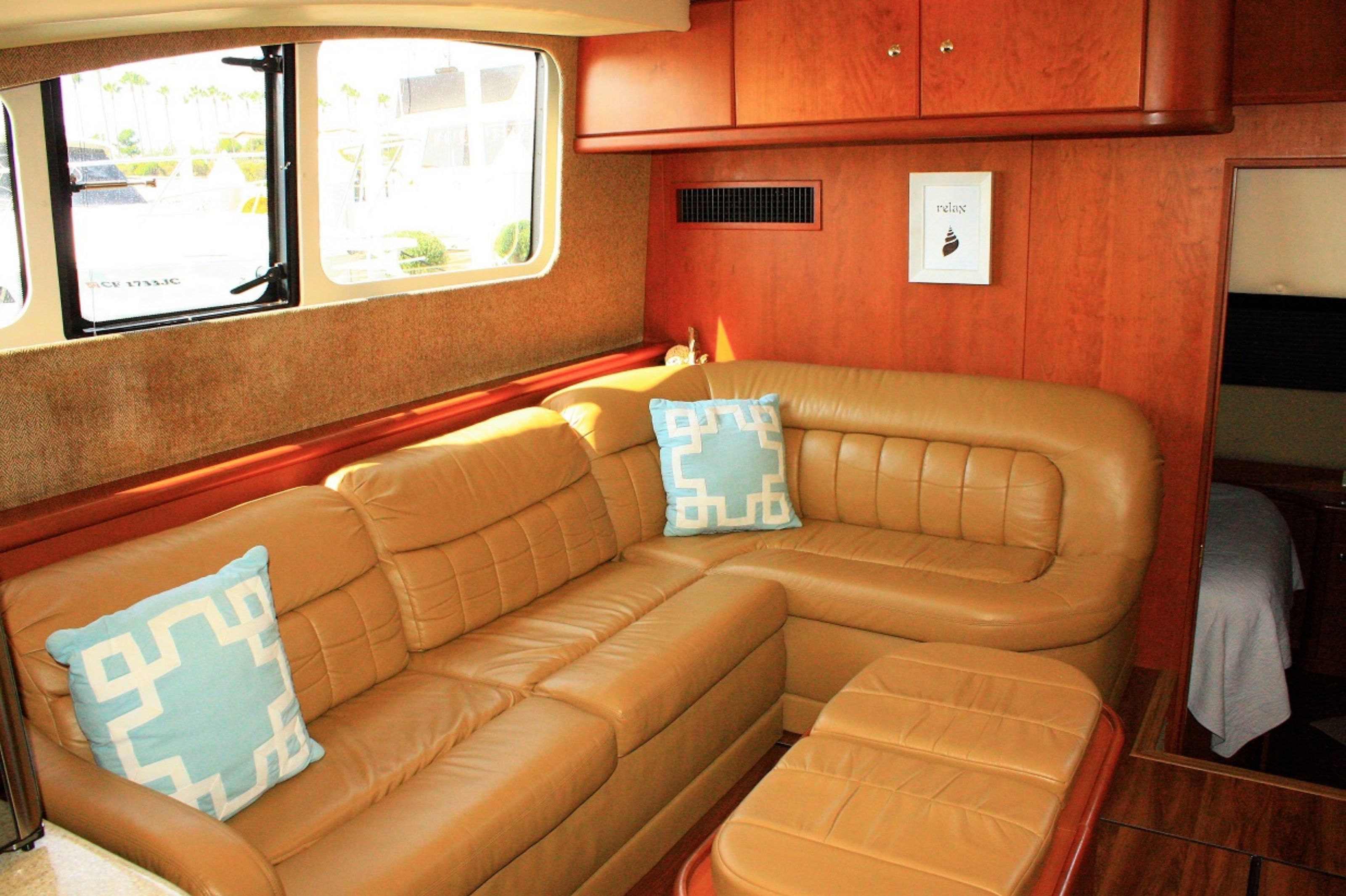 A cozy interior with a leather sofa and cushions, wooden cabinetry, and a window providing a view of the outside.