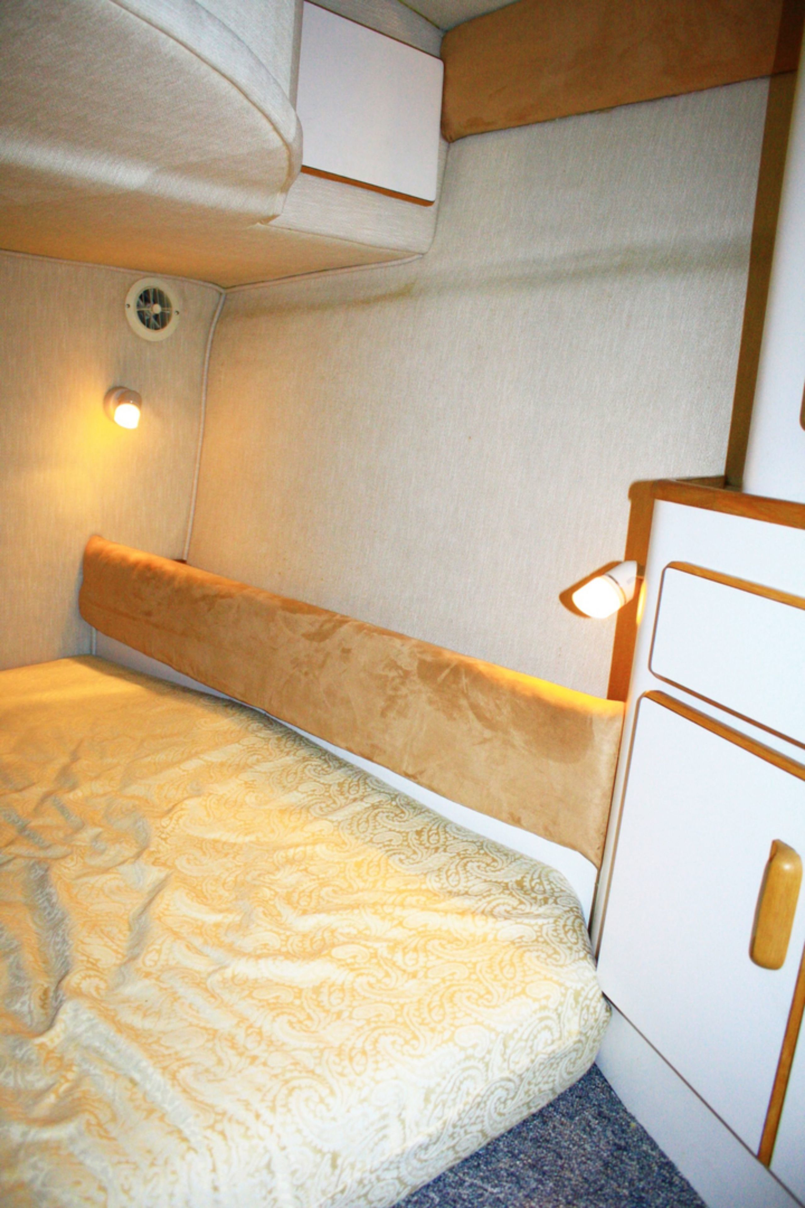 A bunk bed with a patterned mattress and a headboard, a small cabinet with a handle, and a wall-mounted light fixture.
