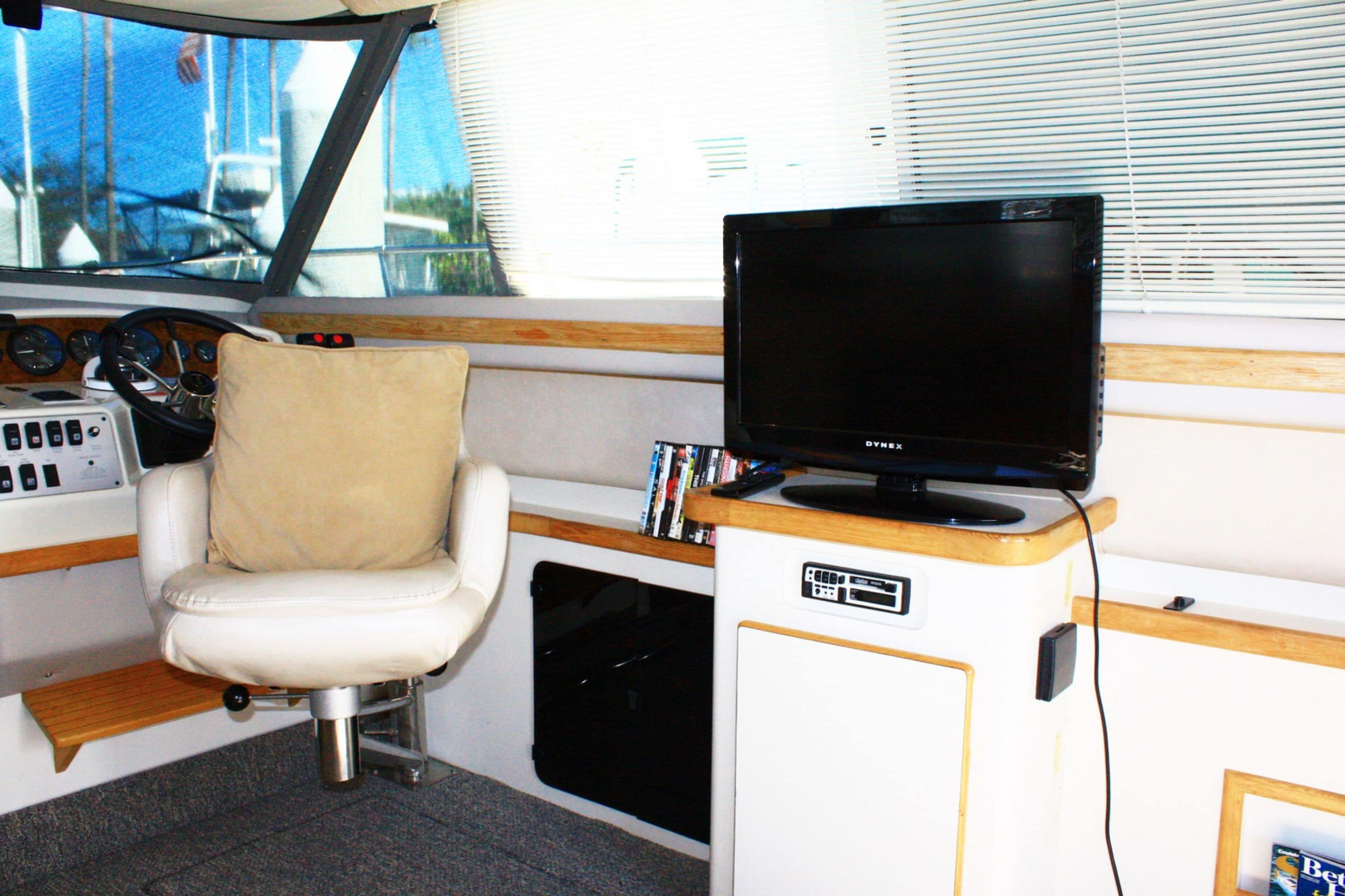 Bootinterieur met een stuurwiel, een beklede zitplaats, een bedieningspaneel en een televisie op een houten voet.