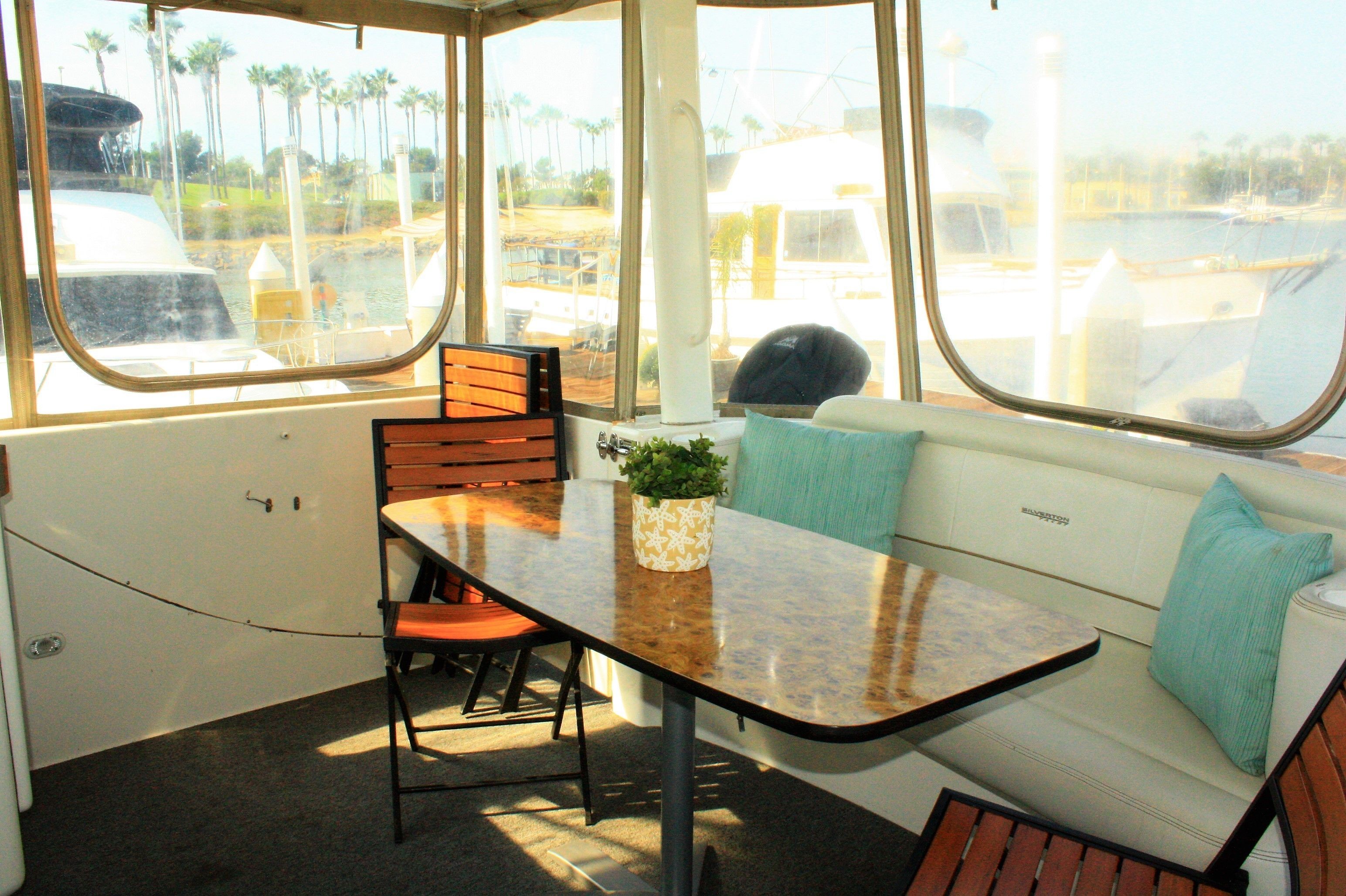 Un interior luminoso con una mesa, sillas y un sofá junto a un ventanal con vistas a un puerto deportivo.