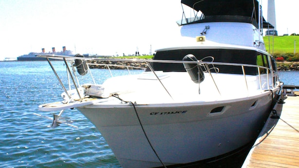 Un yate blanco amarrado en un muelle, con un faro al fondo.