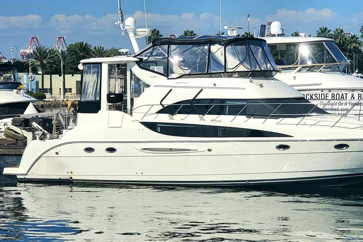 A large yacht docked at a marina with a clear view of the surrounding palm trees and buildings.