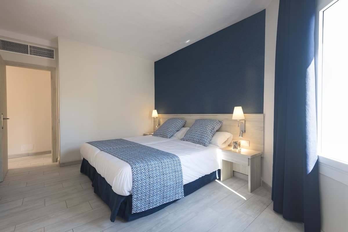 A modern bedroom with a large bed, bedside lamps, and a view of the outdoors.