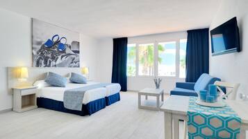 Une chambre d’hôtel équipée d’un lit, d’un bureau, d’une chaise, d’une télévision et d’une fenêtre donnant sur la plage.