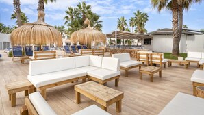 A poolside area with wooden furniture, white cushions, and thatched umbrellas. - Aparthotel Marinda Garden (Ciutadella de Menorca)