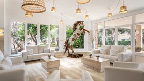A spacious living room with white furniture, large windows, and a decorative horse sculpture. - Aparthotel Marinda Garden (Ciutadella de Menorca)