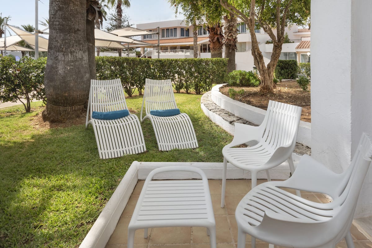 A patio area with white lounge chairs and a small table, surrounded by a well-maintained lawn and a building in the background.