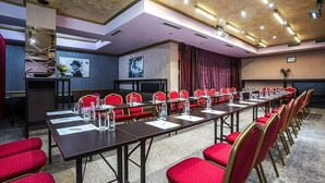 Un salón de conferencias con una larga mesa, sillas rojas y una pantalla para proyector.