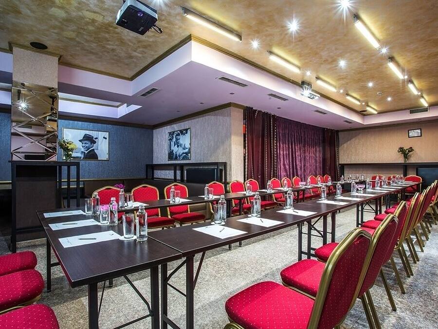 Un salón de conferencias con una larga mesa, sillas rojas y una pantalla para proyector.