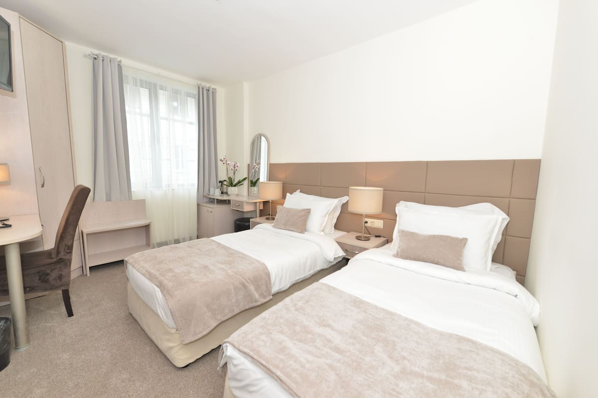 A hotel room with two beds, a desk, a chair, and a mirror.