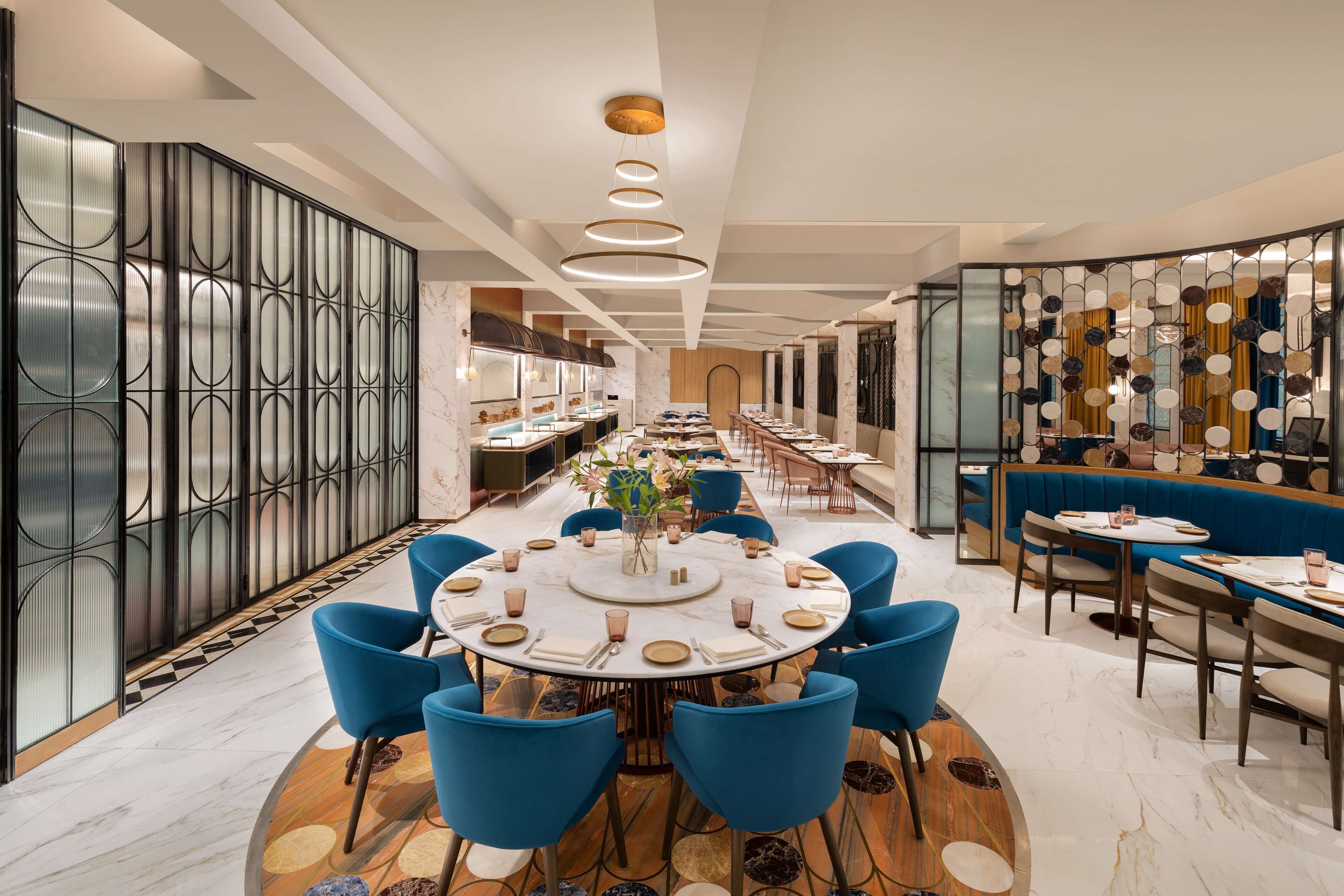 A modern dining area with a round table, blue chairs, and a decorative wall with circular patterns.