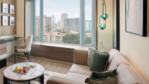 A modern living room with a large window, a sofa, a coffee table with fruits, and a city view. - Radisson Mumbai Goregaon (Mumbai)
