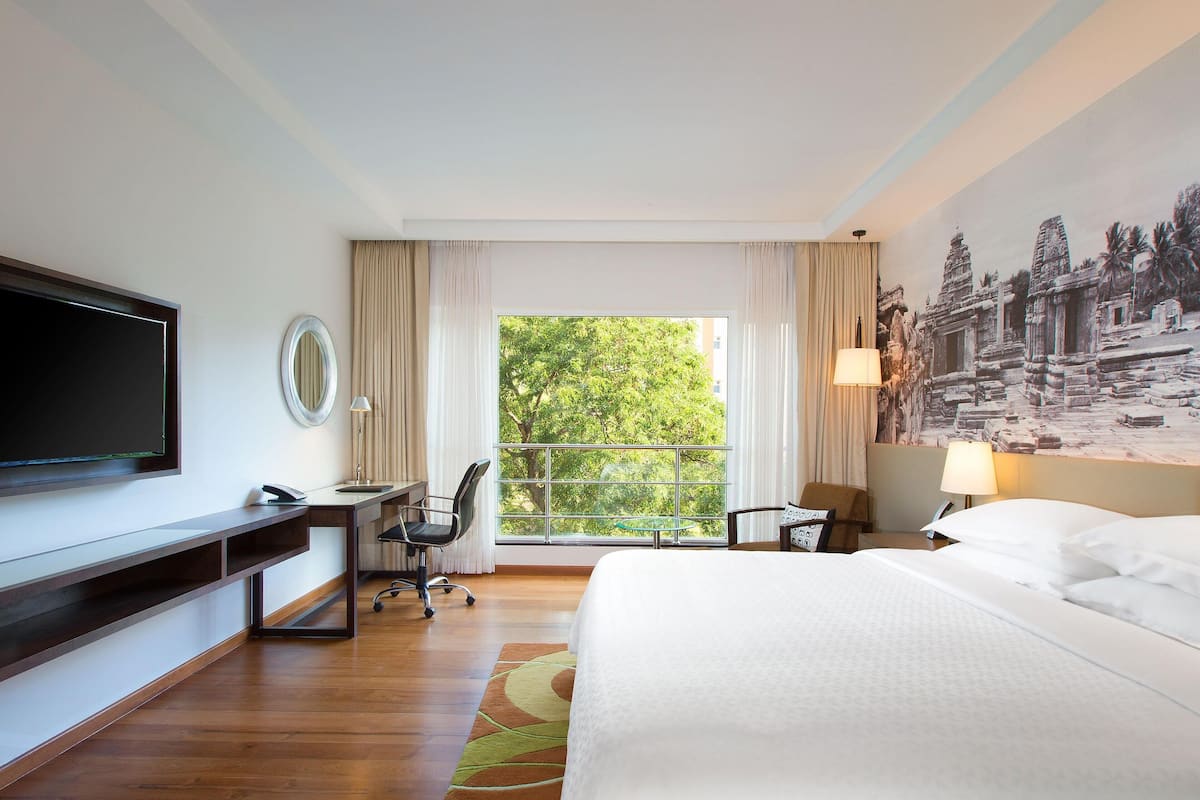 A hotel room with a large bed, a desk with a chair, a television, and a window with curtains.