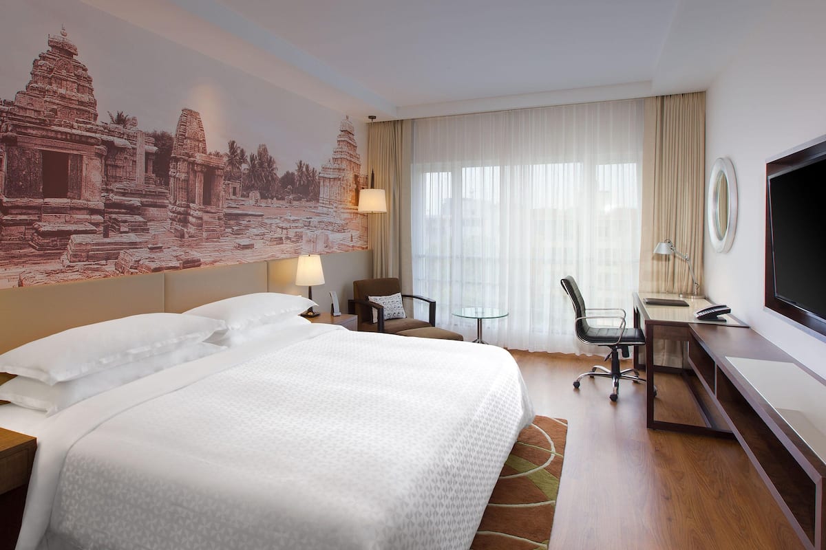 A hotel room with a large bed, a desk with a chair, a television, and a mural of a temple on the wall.