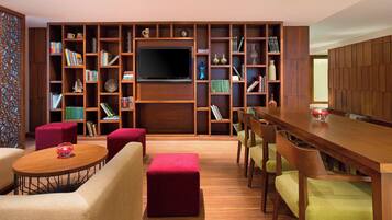 A modern living room with a wooden bookshelf, a flat-screen TV, and a dining area with wooden chairs and a table.