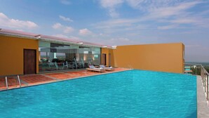 Una piscina infinita en la azotea con sillas de descanso, una zona cerrada con equipo de ejercicios y un cielo despejado.