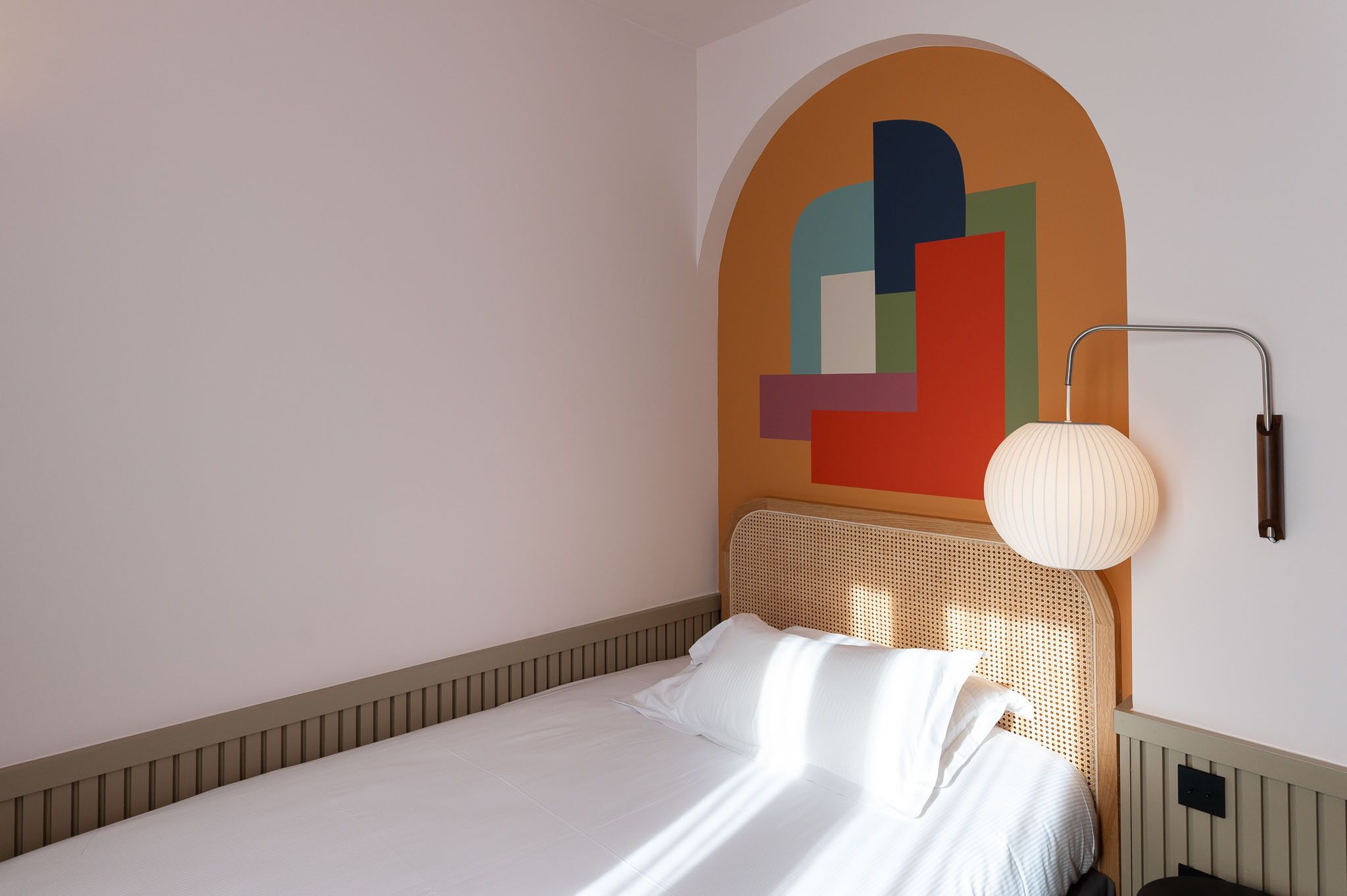 Una cama bien tendida con sábanas blancas en una habitación de diseño moderno y sencillo.