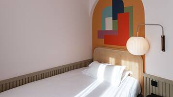 Una cama bien tendida con sábanas blancas en una habitación de diseño moderno y sencillo.