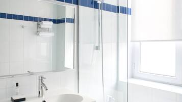 A modern bathroom with a glass-enclosed shower, a white sink, and a large mirror.