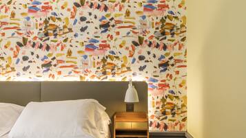 A hotel room with a bed, a nightstand, a lamp, and a wall with a colorful abstract pattern.