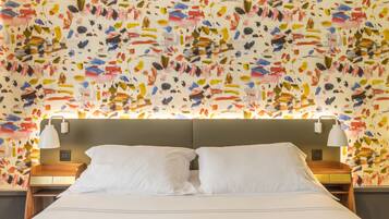 Una habitación de hotel con cama, dos mesitas de noche y un llamativo mural abstracto en la pared.