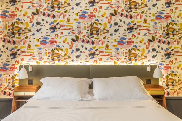 A hotel room with a bed, two bedside tables, and a colorful abstract wall mural.