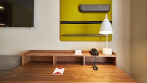 Una habitación de hotel moderna con un escritorio de madera, un televisor de pantalla plana montado en la pared, una lámpara de escritorio, un teléfono y un bloc de notas.