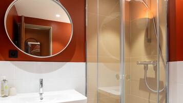 A bathroom with a white sink, a round mirror, and a glass-enclosed shower area.
