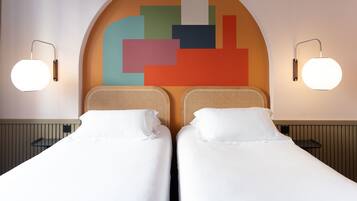 A hotel room with two beds, a colorful abstract wall art, and two wall-mounted lamps.