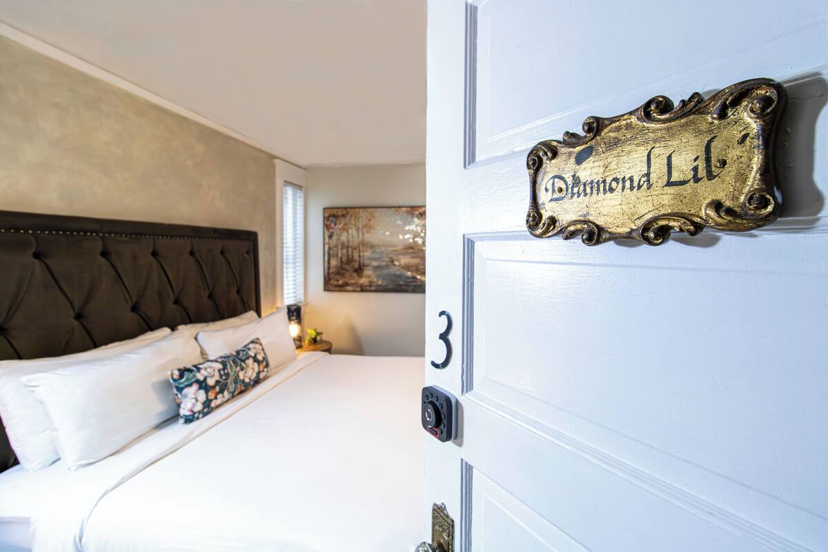 A hotel room with a bed, a headboard, a door with a number, and a sign reading "Diamond Lil".