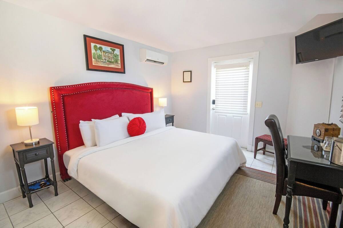 A hotel room with a large bed, a desk with a chair, a television, and a door with blinds.