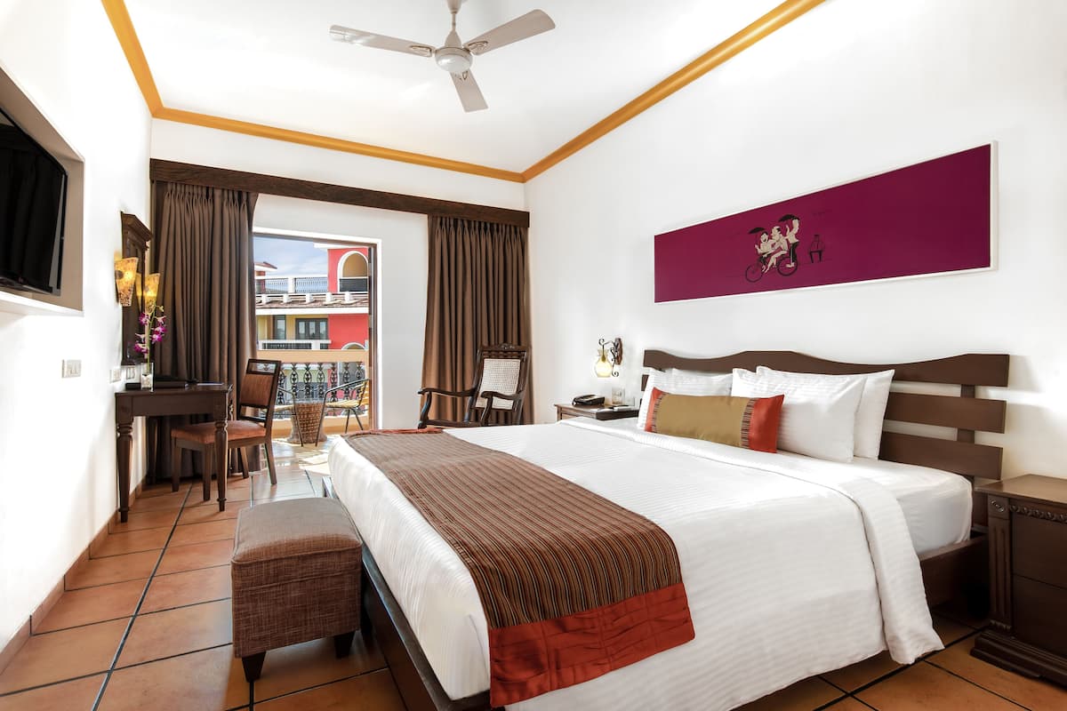 Habitación de hotel con cama, escritorio, silla, televisor y ventana con cortinas.